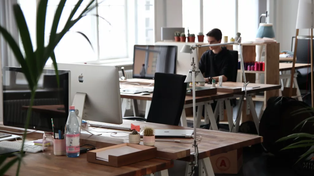An office with several laptops, desks and a person working in the background