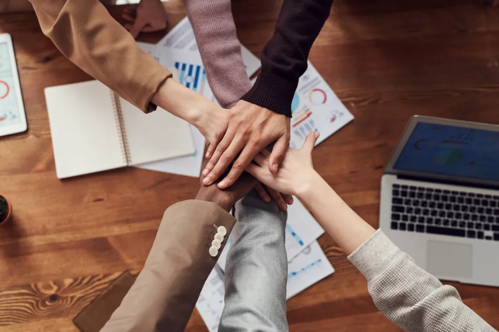 people holding hands with paper documents on a desk below them